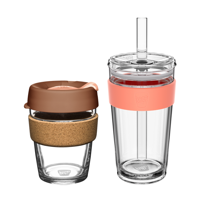 KeepCup Booked & Busy Frappe set featuring two reusable cups: a glass coffee cup with cork band and brown lid alongside a larger clear tumbler with coral-coloured silicone band and straw, shown against a white background.