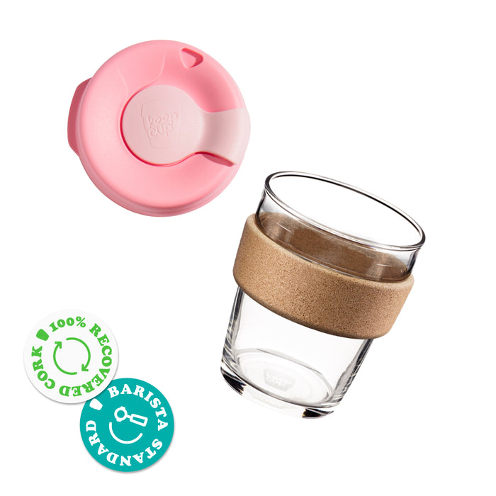 KeepCup Brew Cork reusable coffee cup shown in an exploded view with pink lid separated from the clear glass cup featuring a natural cork band, alongside badges indicating 100% recovered cork and barista standard sizing.