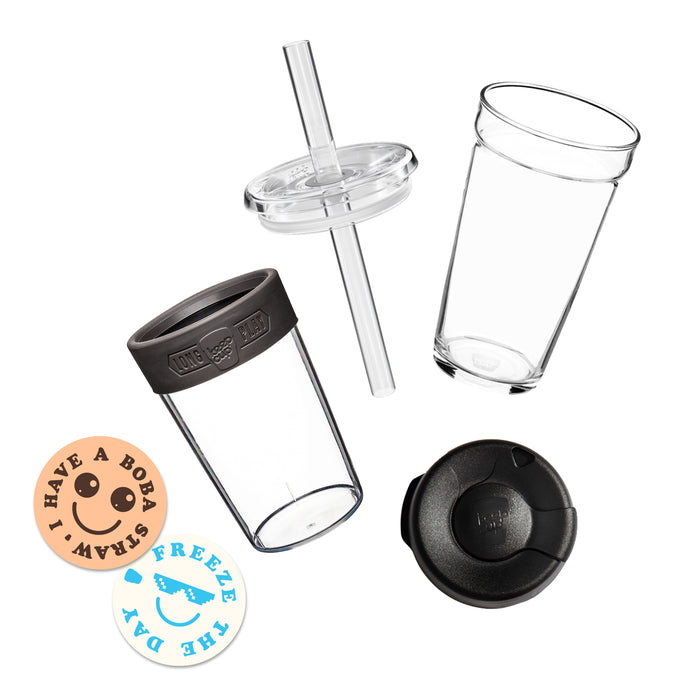 Exploded view of the Cold Cup Longplay showing the clear glass cup, charcoal-coloured silicone band with "Long Play KeepCup" embossing, plastuc outer sleeve, clear lid with boba straw, and a circular peach sticker reading "I have a boba straw" with a smiley face and "Freeze The Day".