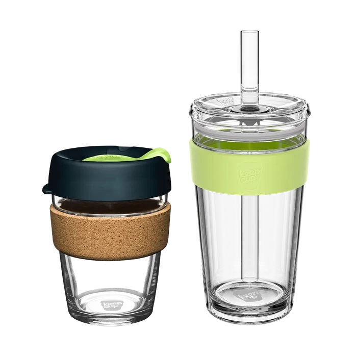 KeepCup Booked & Busy | Deep set featuring two reusable cups: a smaller glass cup with cork band and dark lid with green accent, and a taller clear tumbler with light green silicone band and straw lid, shown side by side on a white background.