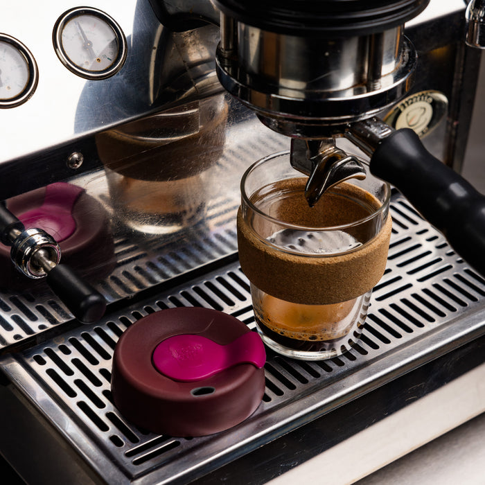 KeepCup Brew Cork M 12oz in Nutmeg sits on an espresso machine drip tray, filled with freshly pulled coffee, with its burgundy and pink silicone lid resting beside it.