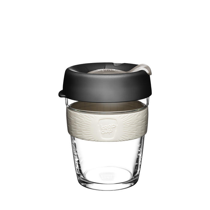 KeepCup Brew M 12oz in Press colour, featuring a clear glass cup with a cream-coloured silicone band and charcoal lid with sipper closure, shown against a white background.
