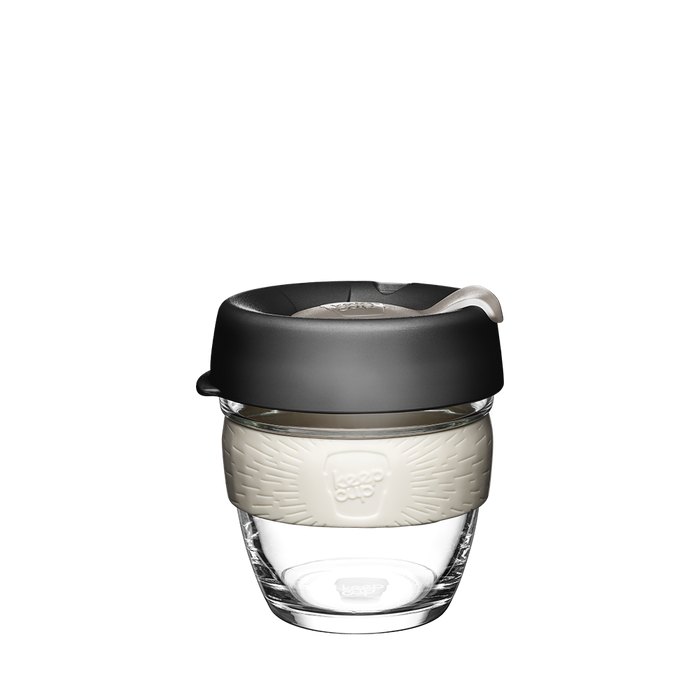 KeepCup Brew S 8oz in Press colour, featuring a clear tempered glass cup with cream-coloured silicone band and charcoal lid with sipper, shown against a white background.