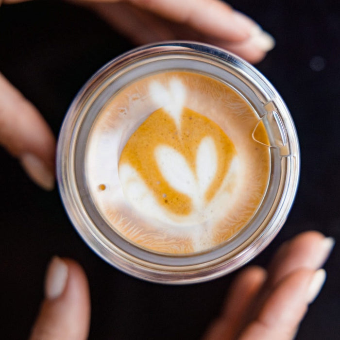 Hands cradling a KeepCup Thermal Quicksip XS 6oz in Rose, viewed from above, showing a latte with a tulip milk art design through the open drinking hole.