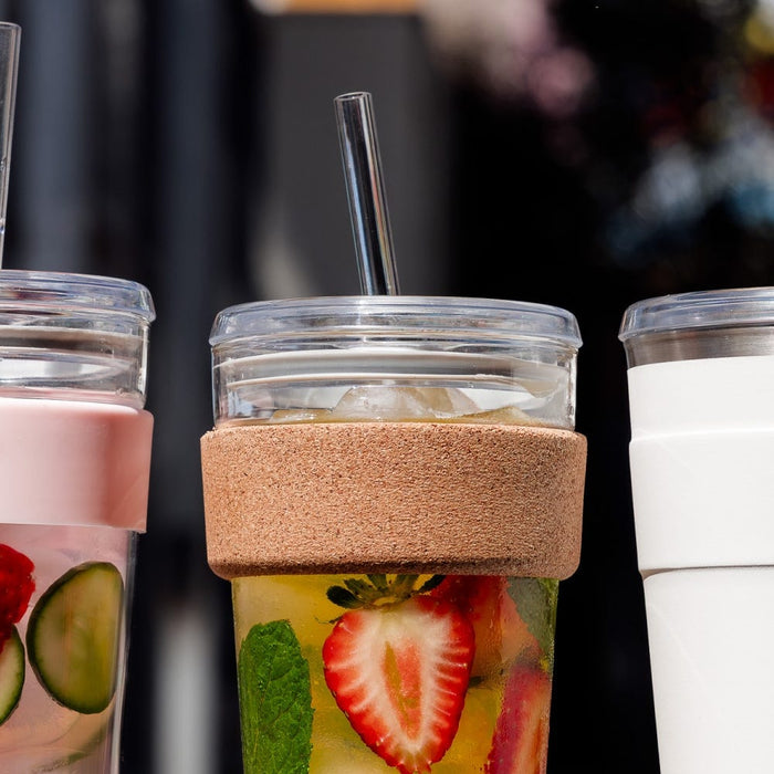 KeepCup Cold Cup Cork M 12oz with Coffee Straw, shown in centre alongside two other reusable cups, filled with fruit-infused water featuring strawberry slices and mint, with a plastic straw inserted through the clear lid.