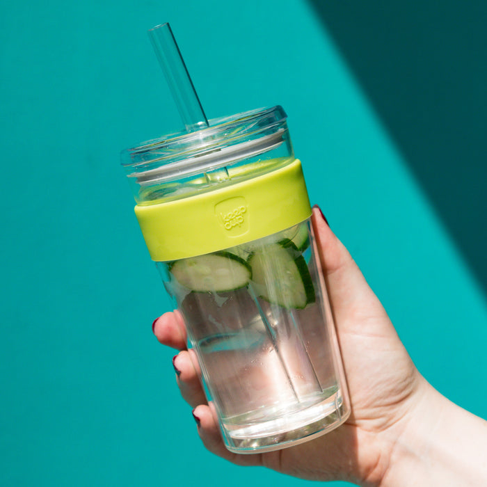 Hand holding a KeepCup Cold Cup Longplay Boba L 16oz in Matcha colour against a teal background, featuring the clear double-walled glass cup with lime green silicone band, filled with cucumber-infused water and a reusable straw.
