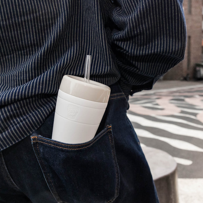KeepCup Commuter Cold Cup M 12oz in Bone colour tucked into the back pocket of dark denim jeans, with a clear straw visible, demonstrating the cup's compact and portable size.