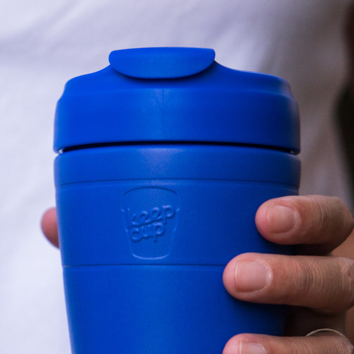 A hand holds the KeepCup Commuter S 8oz in Electric Blue, showcasing the vibrant matte blue reusable cup with matching lid and embossed KeepCup logo on the band.