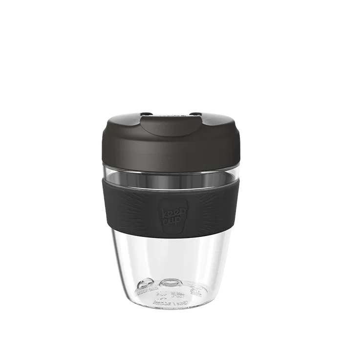 KeepCup Commuter Light M 12oz in Black, shown against a white background. The reusable cup features a clear lightweight plastic body, dark charcoal lid with sipper spout, and matching black silicone band with embossed KeepCup logo.