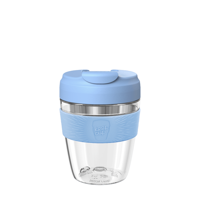 Clear reusable coffee cup with a blue lid and sleeve on a green background
