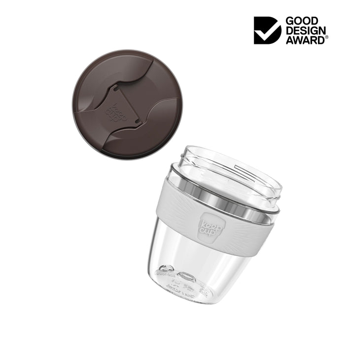 KeepCup Commuter Light M 12oz shown as an exploded view with lid separated above the clear plastic cup featuring a light grey silicone band. Good Design Award logo displayed in corner.