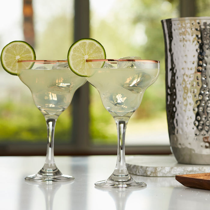 Two margarita glasses with copper colored rim setting on counter next to pitcher.