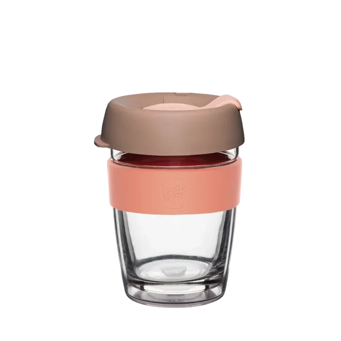 KeepCup Brew Longplay in Canna, medium 12oz size, shown against a white background. The reusable coffee cup features a clear double-walled glass body, peach-coloured silicone band with embossed KeepCup logo, and a taupe-toned lid with sipper opening.