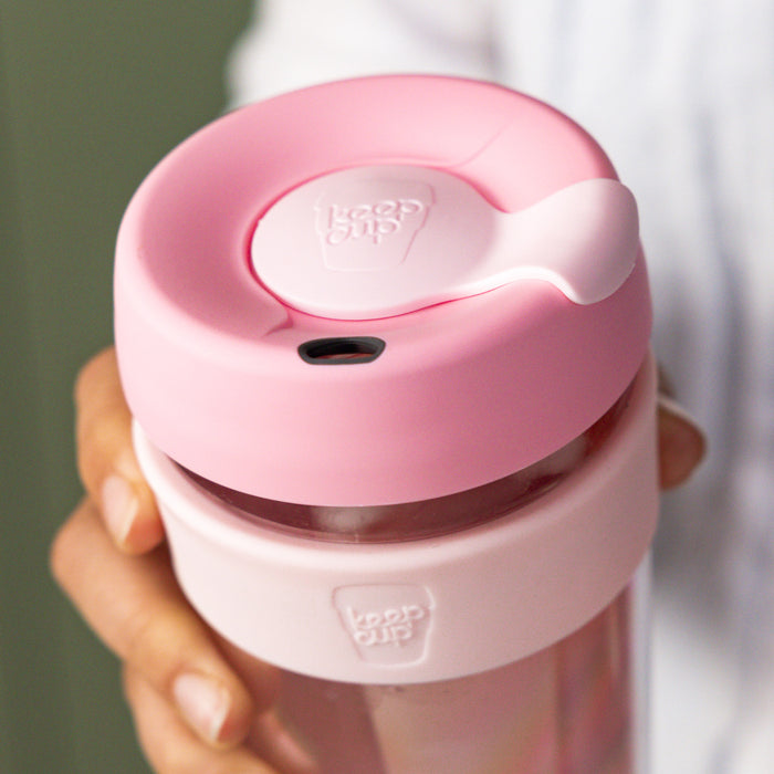Hand holding a KeepCup Brew Longplay M 12oz in Pashmak Pink, showing the pink plastic lid with sipper plug and light pink band around the glass cup, viewed from above at a slight angle.