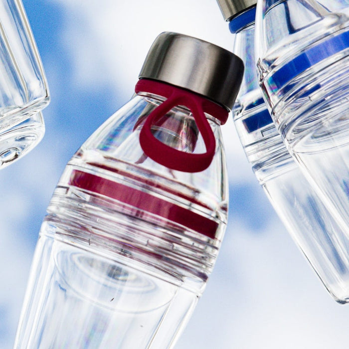 Glow Getter Burgundy reusable bottle photographed from below against a blue sky, showcasing its clear body with burgundy silicone carry loop and accent band, alongside other colour variants in the range.