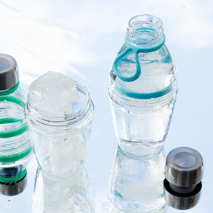 KeepCup Glow Getter in Cloud colour displayed with other reusable bottles on a reflective wet surface, showing the clear cup with ice inside alongside its teal carrying loop and grey lid components.