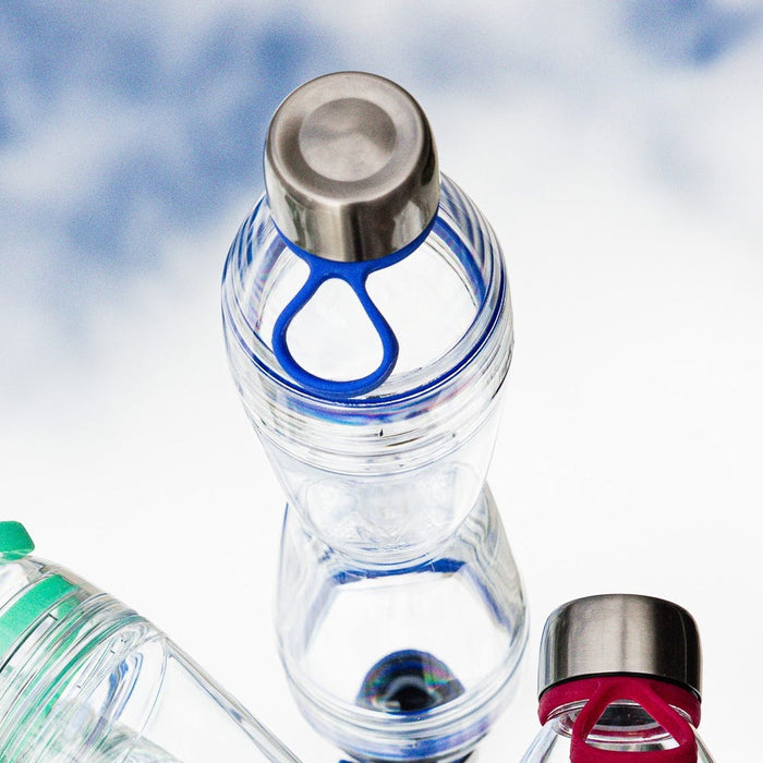 Clear reusable KeepCup bottle with stainless steel cap and blue carrying loop, shown alongside other bottle variants with green and red accents, photographed from above against a soft white background.