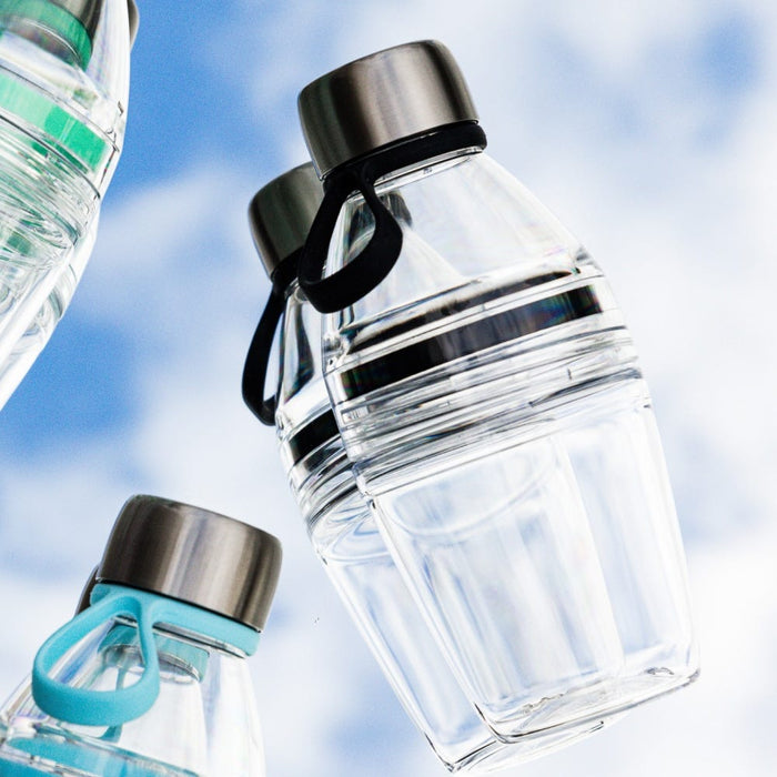 Clear reusable KeepCup bottles photographed from below against a blue sky, featuring the Glow Getter Pine variant with black carry loop and stainless steel lid, alongside other colour options with teal and green accents.
