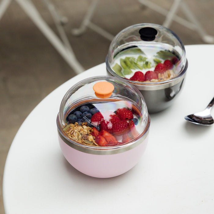 Two yogurt containers with fruit and granola on a white surface.