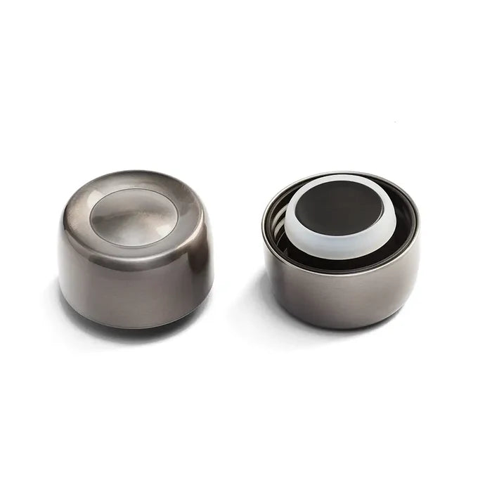 Two Helix Bottle Cap components in Nitro finish shown side by side—one displaying the brushed stainless steel exterior with recessed centre, the other revealing the internal mechanism with white silicone seal and black inner cap.