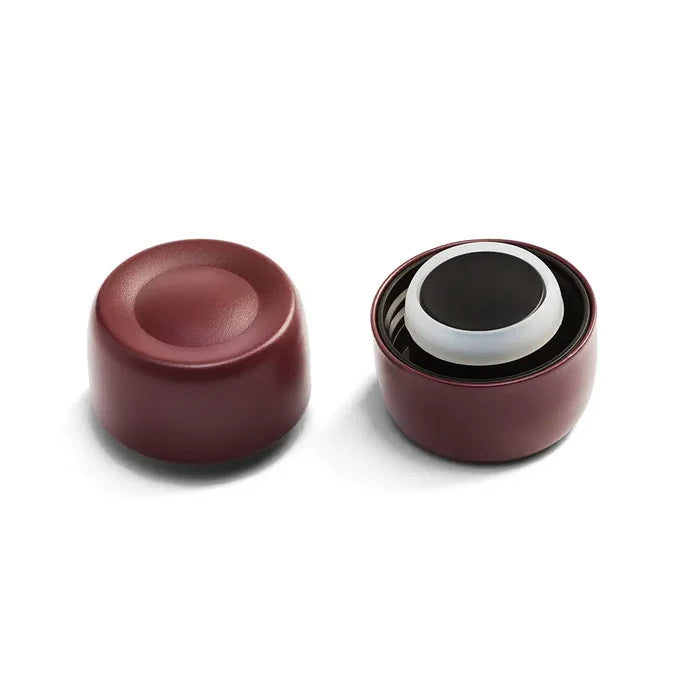 KeepCup Helix Bottle Cap in Plum shown from two angles: the left displays the cap's smooth exterior with circular indentation, while the right reveals the interior components including the white silicone seal and black lid mechanism.