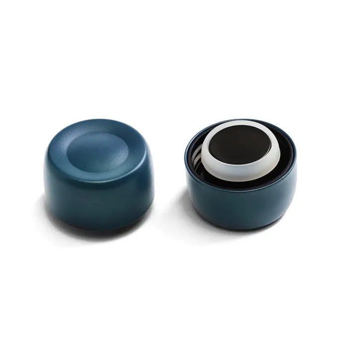 KeepCup Helix Bottle Cap in Storm colour shown from two angles: the cap base with its concave underside on the left, and an exploded view on the right displaying the internal components including the white silicone seal and black lid nested inside the dark teal outer shell.