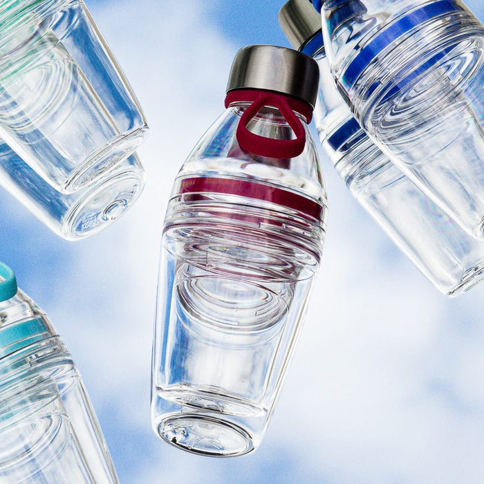 KeepCup Helix Light Bottle 530ml in Burgundy photographed from below against a pale blue sky, featuring a clear body with burgundy accents and carry loop, surrounded by other reusable bottles at dynamic angles.