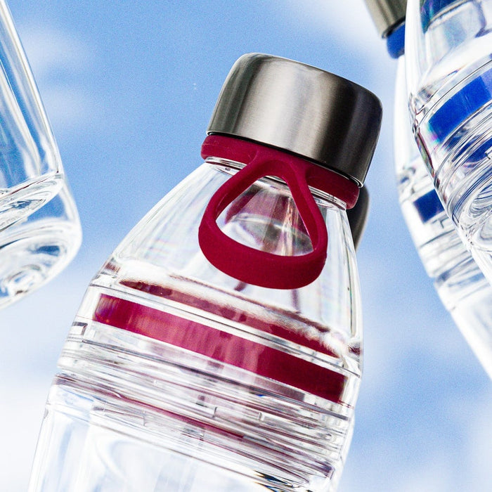 KeepCup Helix Light Bottle 530ml in Burgundy photographed from a low angle against a blue sky, featuring a clear body with burgundy silicone carrying loop and horizontal stripes, topped with a stainless steel lid, with other bottles partially visible on either side.