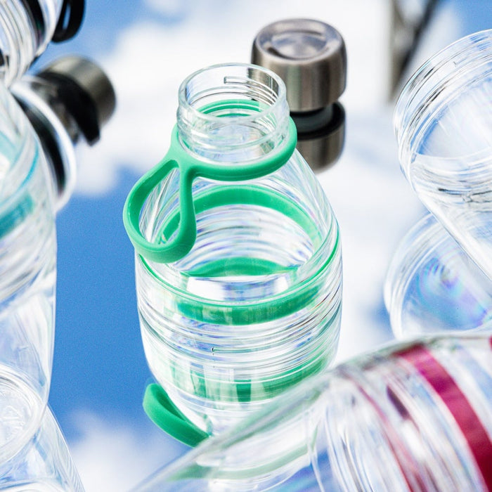 KeepCup Helix Light Bottle 530ml in Frost, a clear reusable water bottle with green silicone carry strap, shown among other bottles against a soft blue sky background.