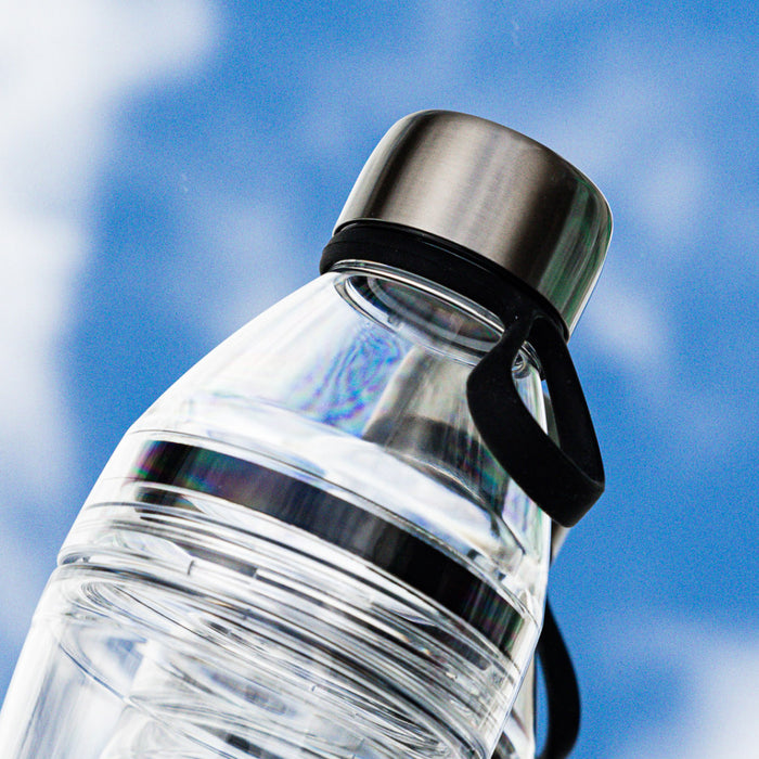 KeepCup Helix Light Bottle in Black, 530ml, shown at a low angle against a blue sky with clouds, highlighting the clear plastic body, stainless steel cap, and black carrying loop.