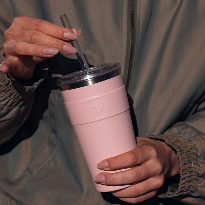 Hands holding a KeepCup Cold Cup Thermal L 16oz in Pashmak Pink, adjusting the reusable straw in the clear lid, with the soft matte pink insulated cup body showing the embossed KeepCup logo.