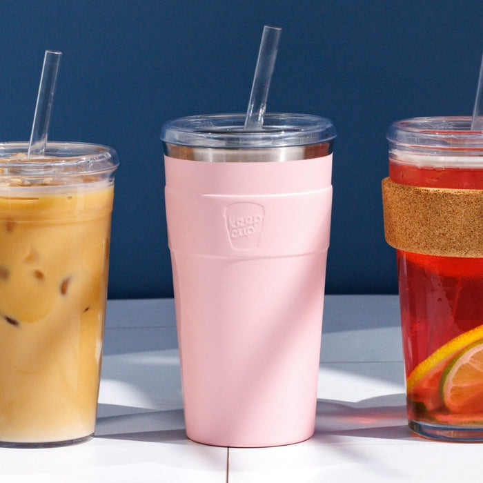 KeepCup Cold Cup Thermal L 16oz in Pashmak Pink, a soft pink insulated tumbler with clear lid and straw, displayed between an iced coffee and a fruit-infused iced tea against a dark blue background.