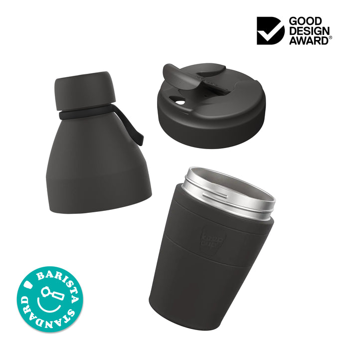 Exploded view of the KeepCup Just Essentials showing three components: the commuter lid, the insulated stainless steel cup body, and the bottle lid with carry loop. Features Good Design Award and Barista Standard certification badges.