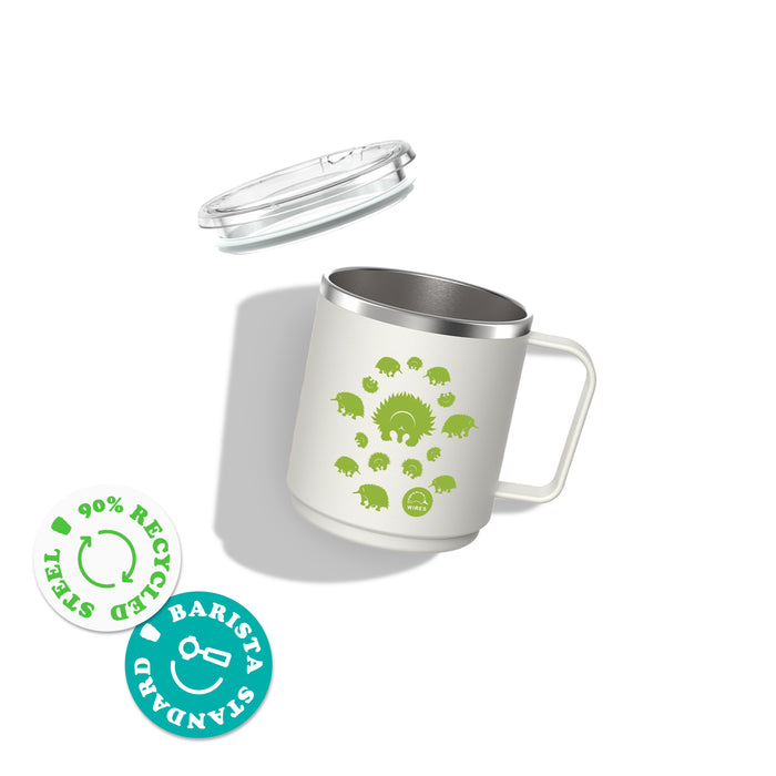 KeepCup x WIRES Camp Mug M 12oz in white with green echidna spiral design, shown with clear lid floating above. The stainless steel interior is visible, alongside badges indicating 90% recycled steel and barista standard compatibility.