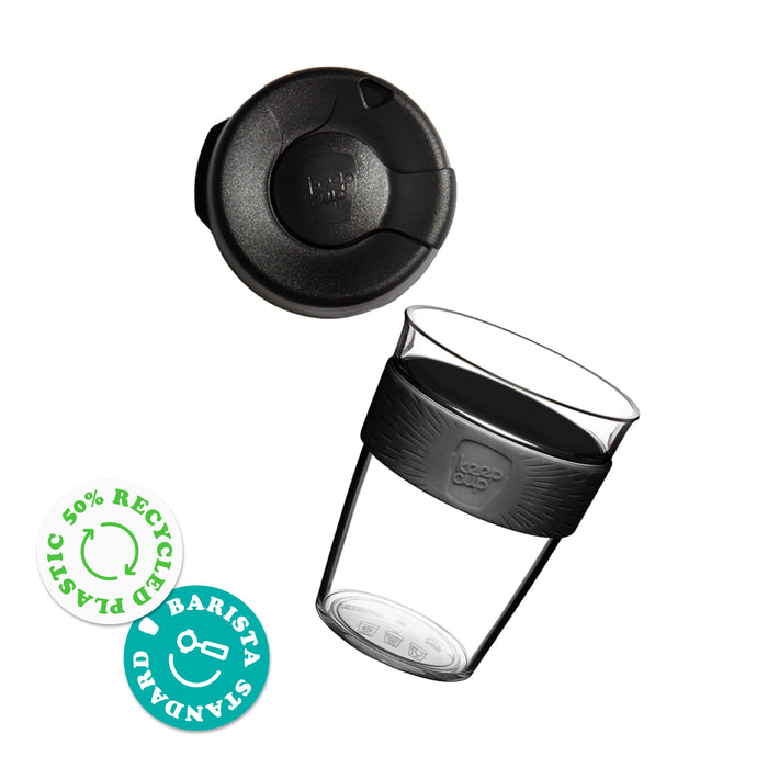 KeepCup Original Clear M 12oz shown as an exploded view with the lid separated from the clear plastic reusable cup featuring a silicone band. Two certification badges indicate 50% recycled plastic and Barista Standard compatibility.