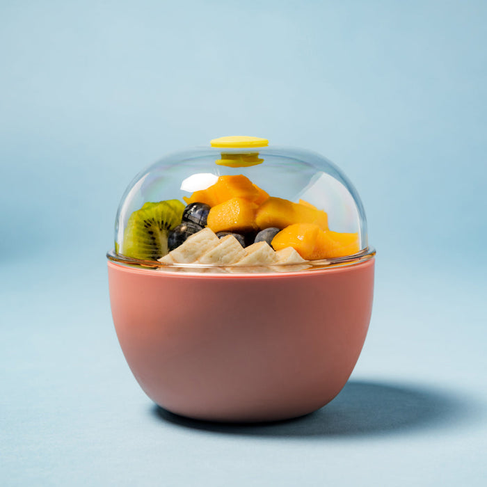 KeepCup Go Bowl Original M 550ml in Clay, featuring a clay rounded base with a clear domed lid and lemon vent button, filled with sliced banana, mango chunks, kiwi and blueberries, photographed against a soft blue background.