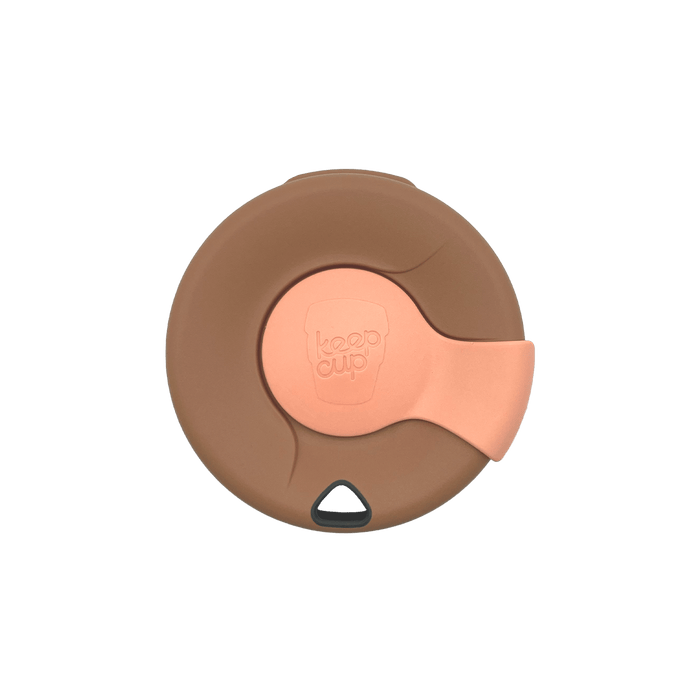 Top-down view of a KeepCup Splashproof Lid in brown with a peach-coloured sipper plug featuring the embossed KeepCup logo, showing the closed drinking position and triangular vent hole.