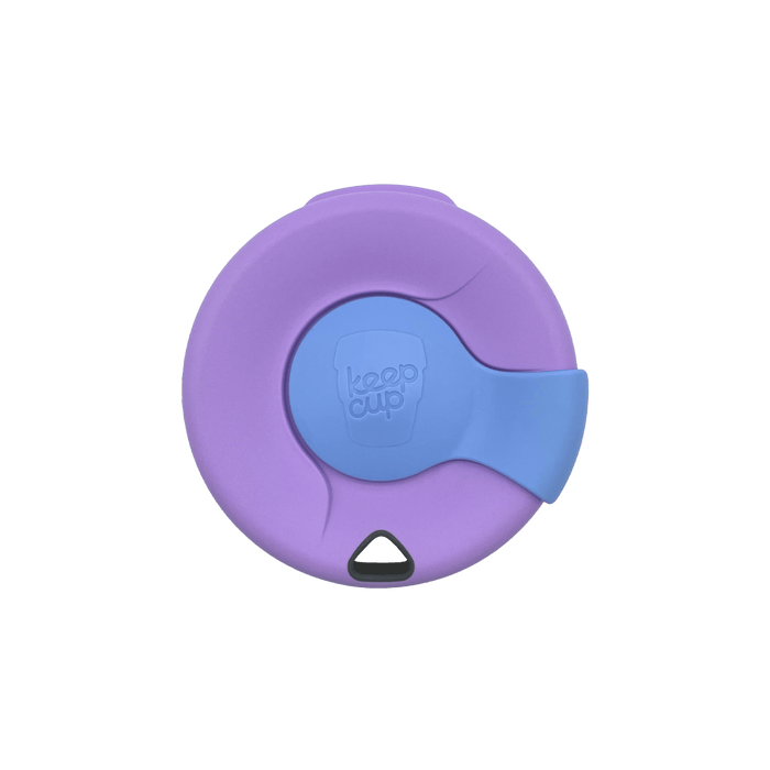 Top-down view of a KeepCup Splashproof Lid in lavender and blue, showing the circular lid with sliding sipper cover embossed with the KeepCup logo and a small triangular vent hole at the bottom.