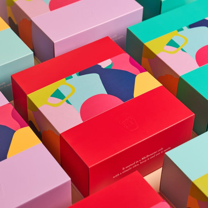 Colourful KeepCup packaging boxes in red, pink, and teal arranged in rows, featuring vibrant abstract illustrations of reusable cups. Text on boxes reads "It started in a Melbourne cafe with a simple idea, keep it and use it again.