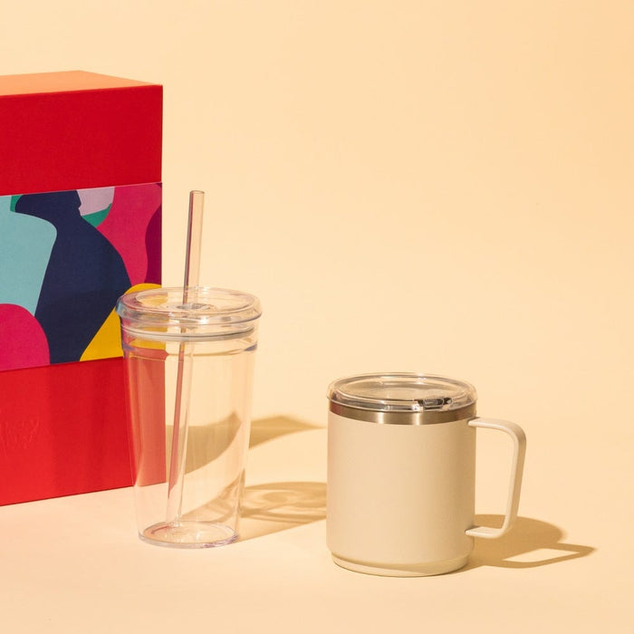 KeepCup Urban Adventurer in Bone, a cream-coloured insulated mug with handle and clear sip lid, displayed alongside a clear double-walled tumbler with straw and colourful gift box packaging on a warm neutral background.
